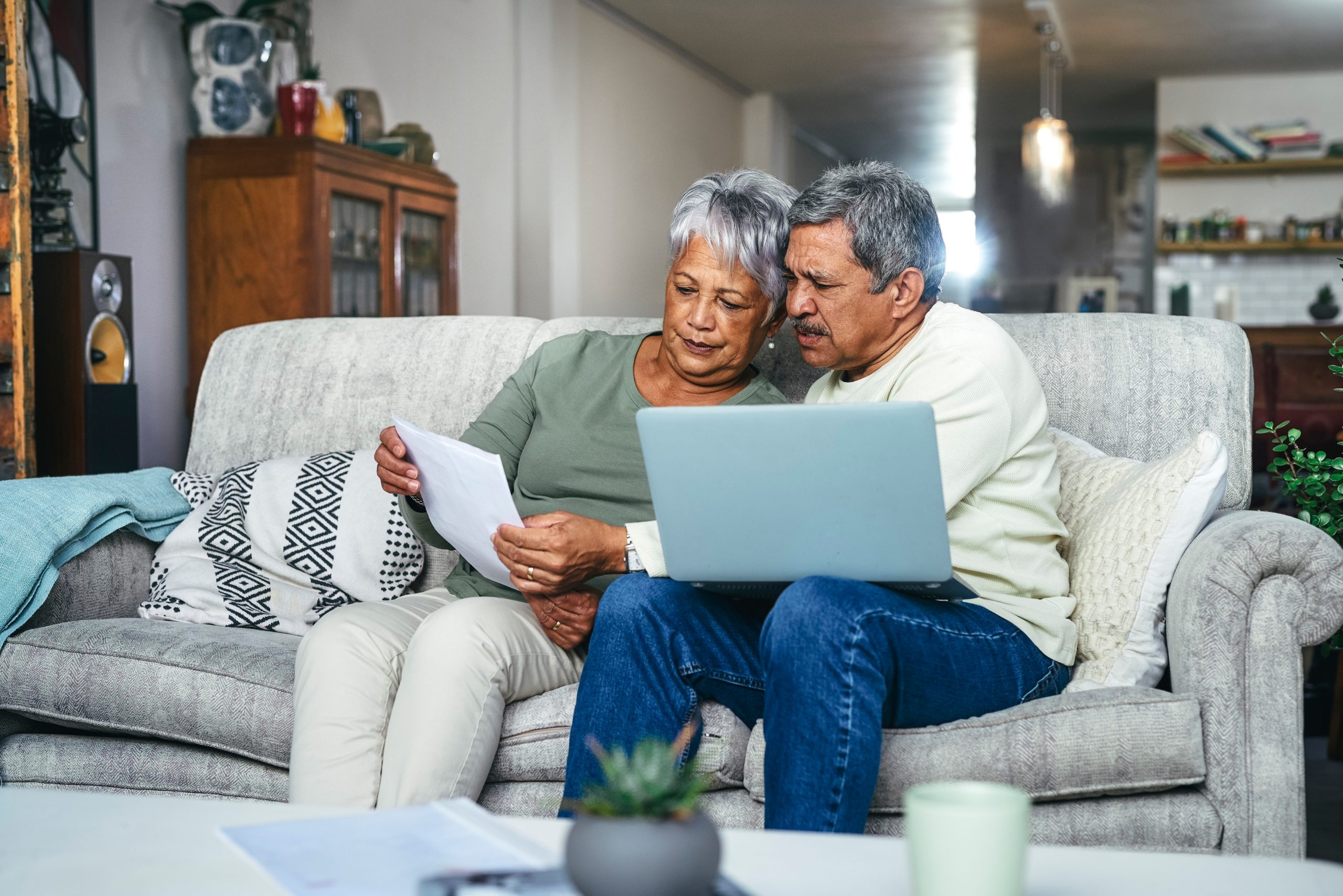 A man and woman sit on a couch looking at paperwork and a laptop. Social Security Disability benefits come in two types: SSDI and SSI.