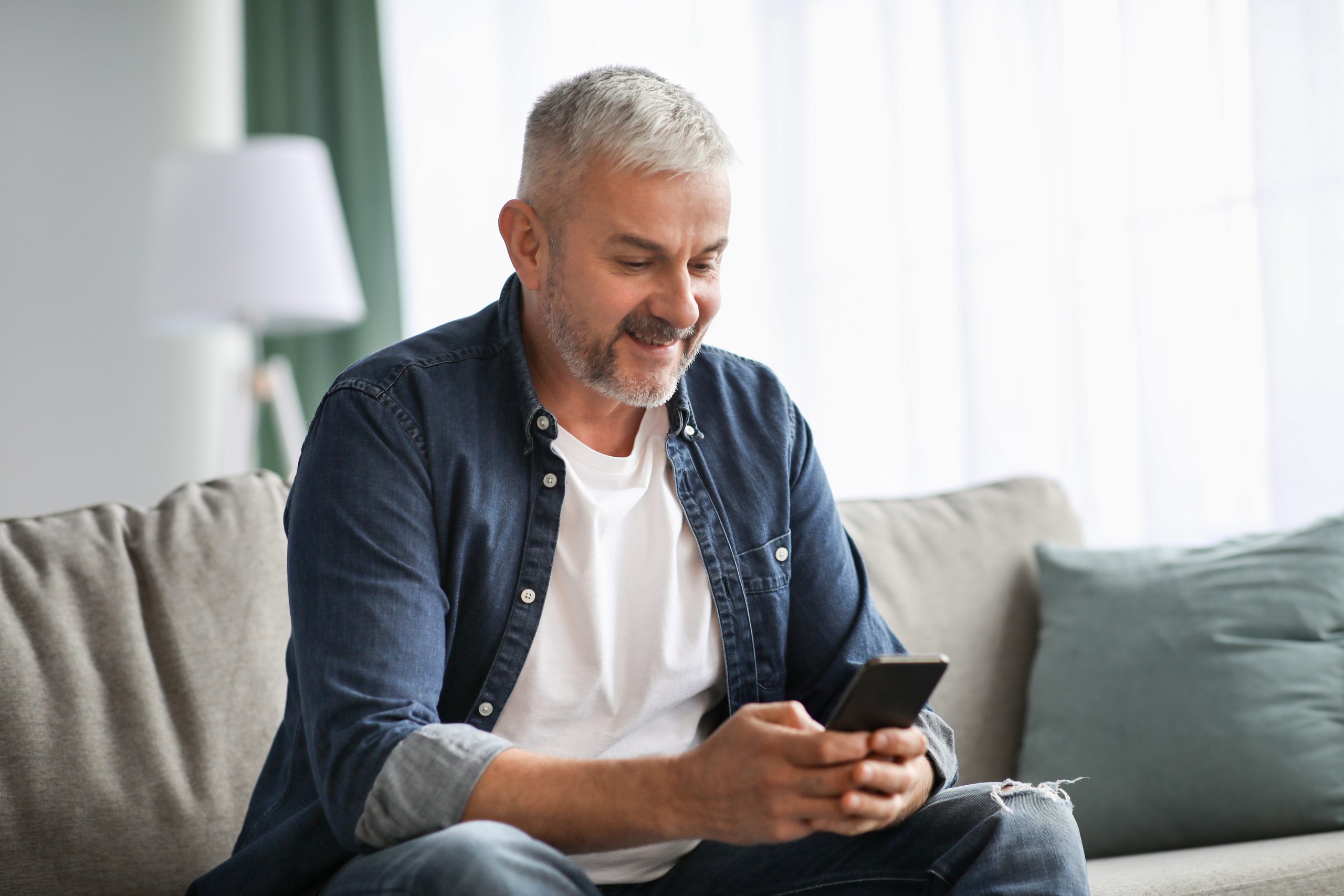 A man smiles while he looks down at his phone. Troutman & Troutman provides local, personal and skilled help with disability benefits claims for people in Tulsa.