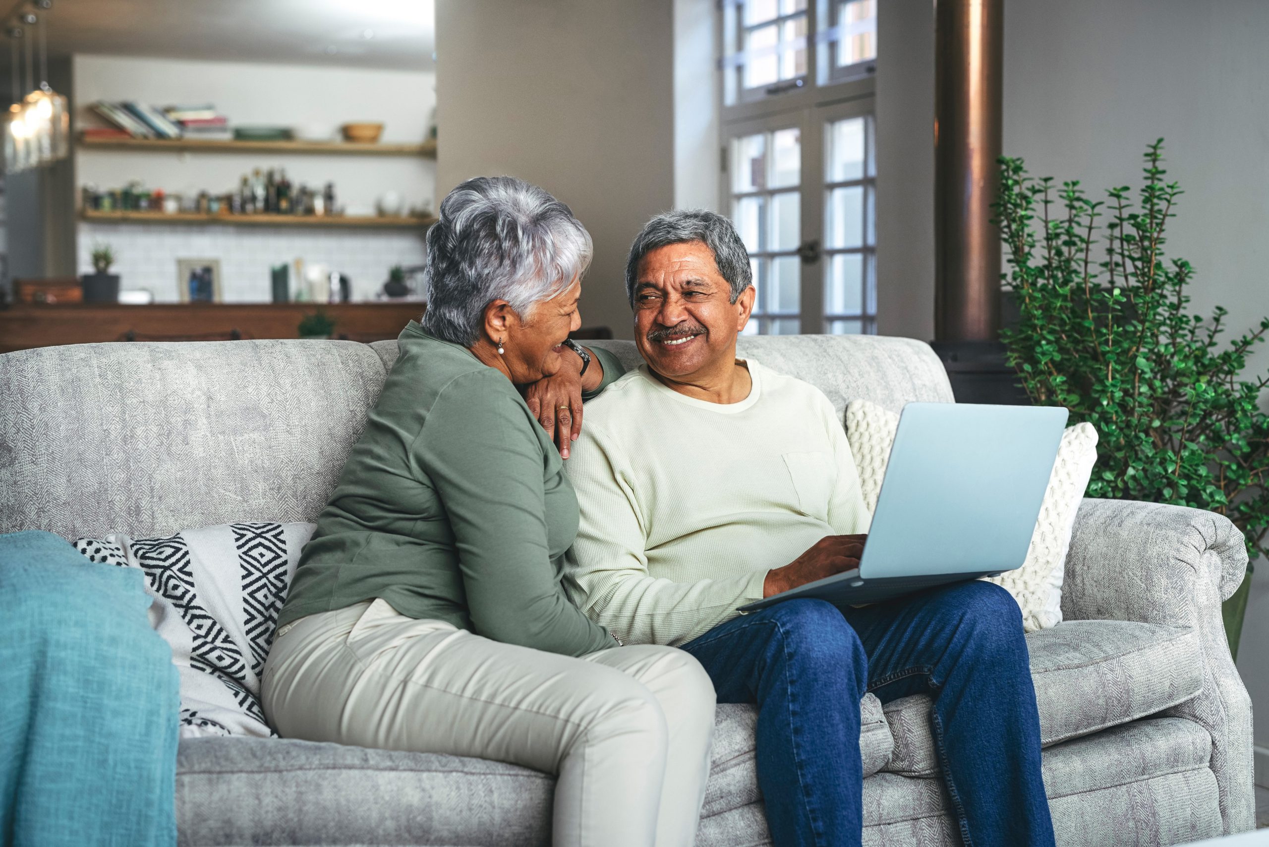A man and woman smile at each other as they sit on a couch. The man holds a computer in his lap. Troutman & Troutman can answer your questions about Social Security Disability benefits.