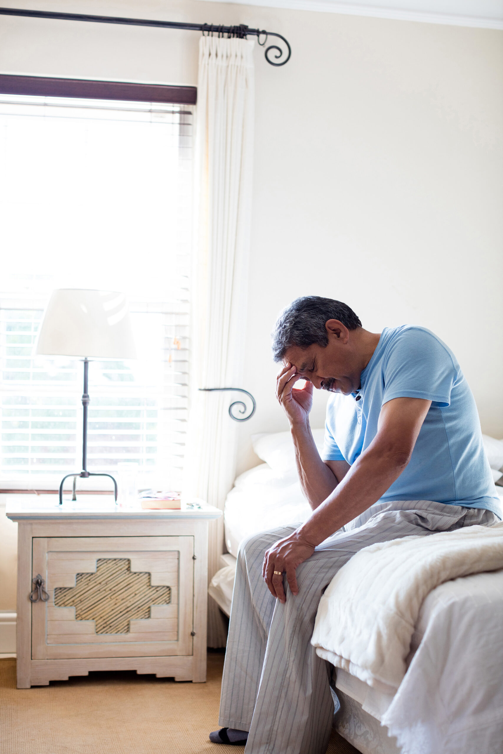 A man sitting at the edge of his bed rests his forehead in his hand and closes his eyes. If you can't work because of health problems, you could get Social Security Disability.