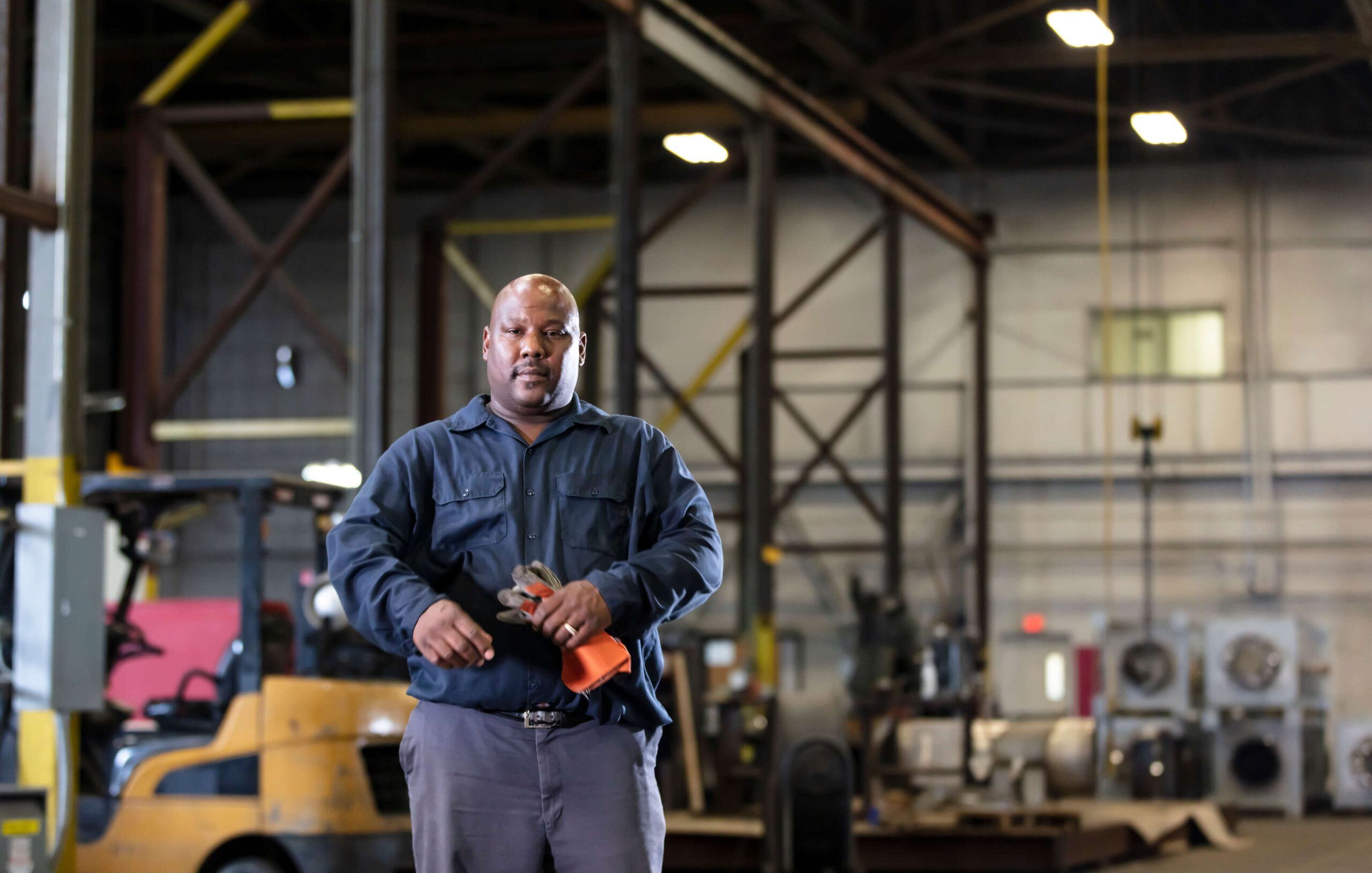 A worker stands in a warehouse holding his work gloves with shelving and equipment in the background. Getting Social Security Disability requires you to have serious health problems.