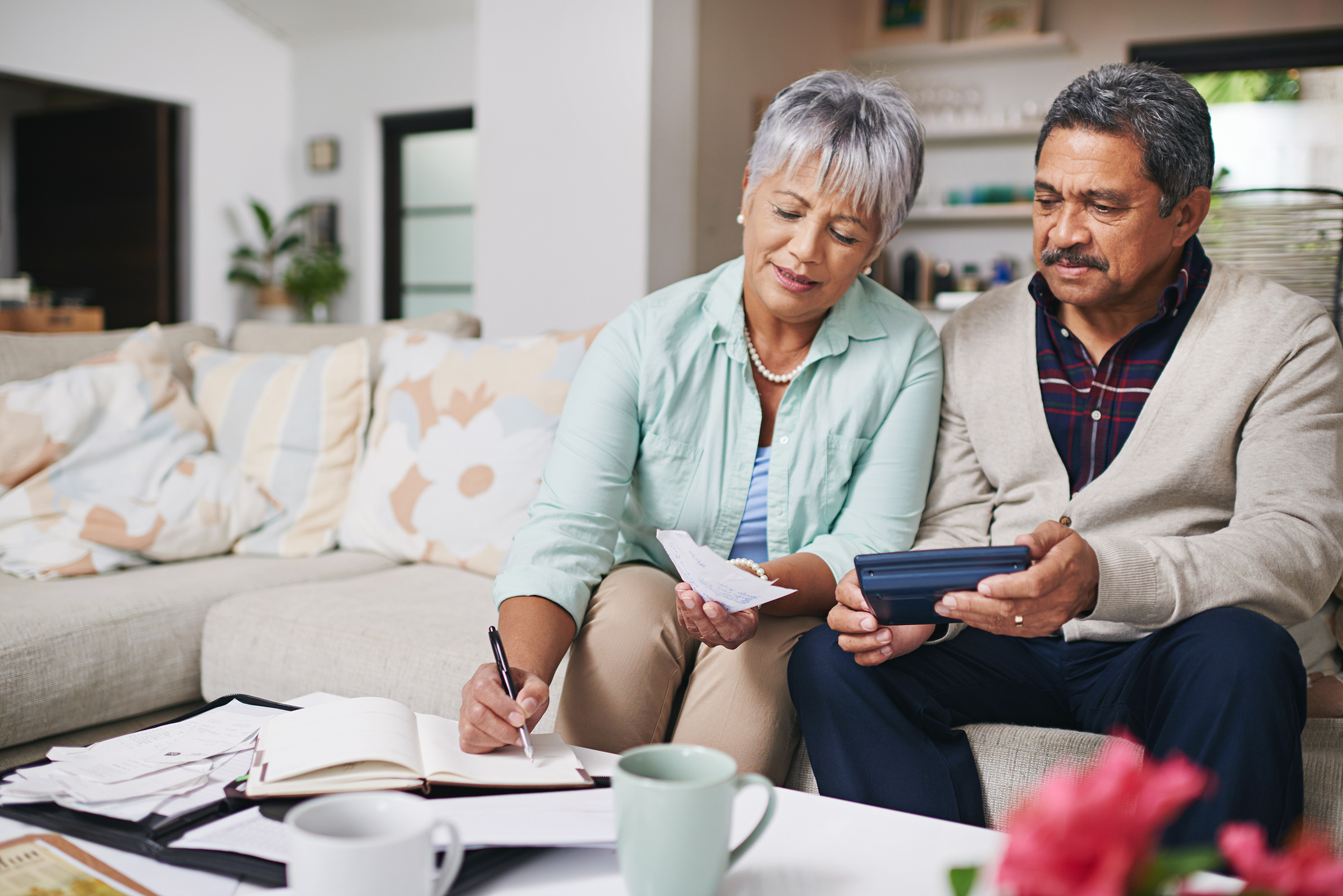 A man and woman sit on a couch looking over notebooks and a calculator. Social Security has a formula for calculating the amount of your disability insurance benefits.