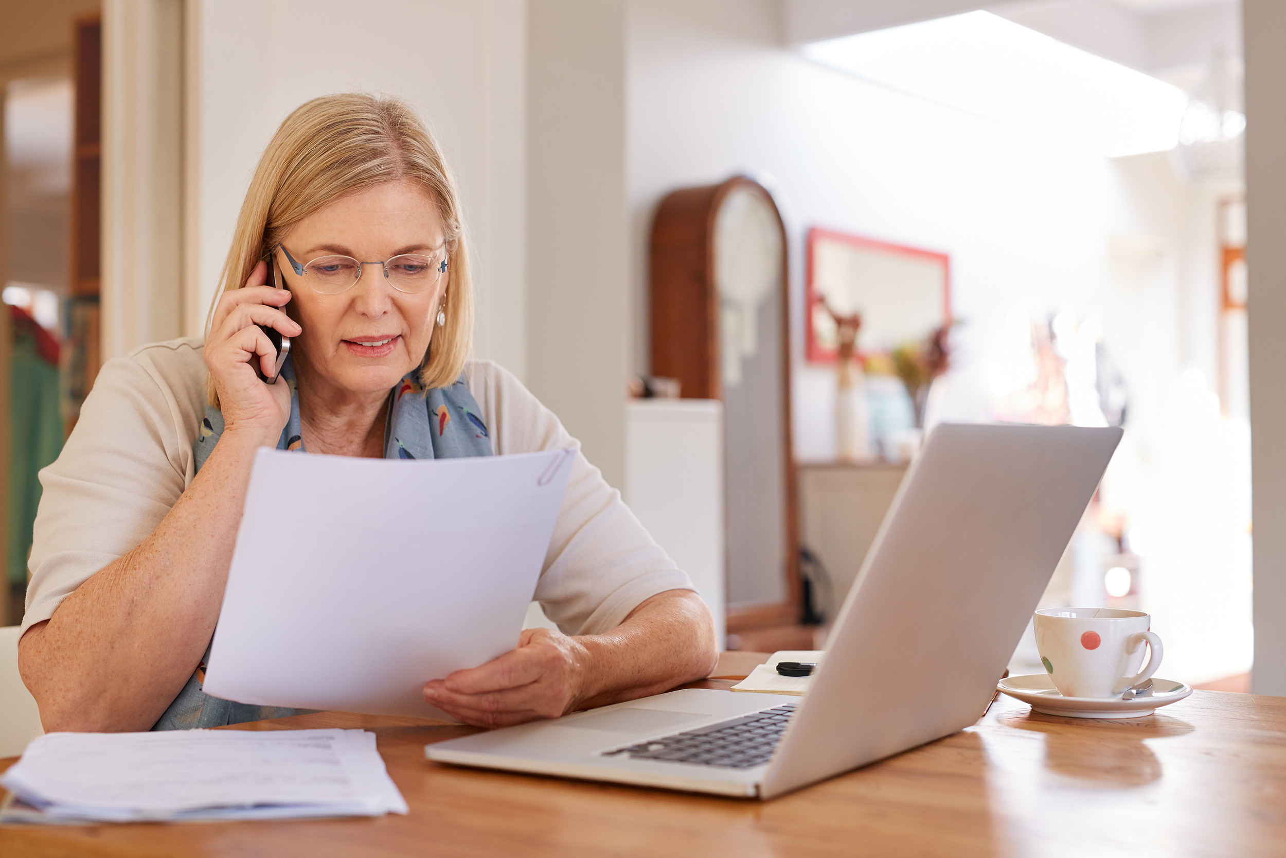 Laptop open and papers in hand, a woman sits at her dining room table talking on the phone. Troutman & Troutman disability attorneys know the common reasons why people get denied for Social Security Disability.