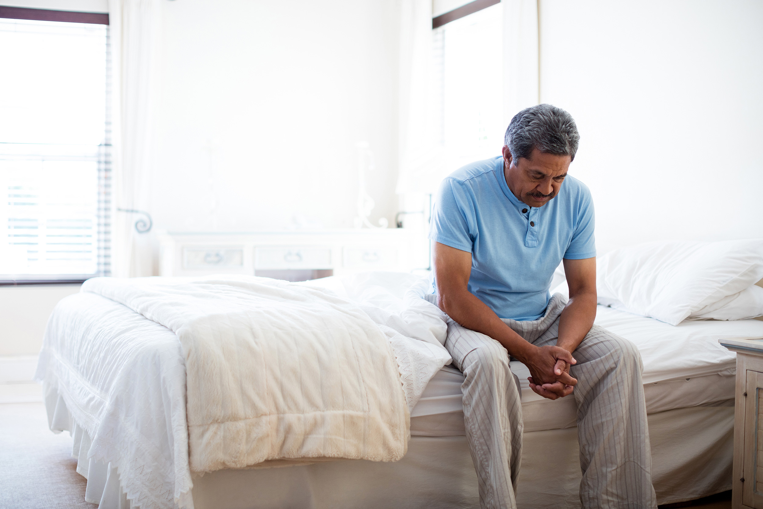 Sitting on the edge of his bed, a man looks down with this hands clasped. It's extremely common to be denied for Social Security Disability benefits.