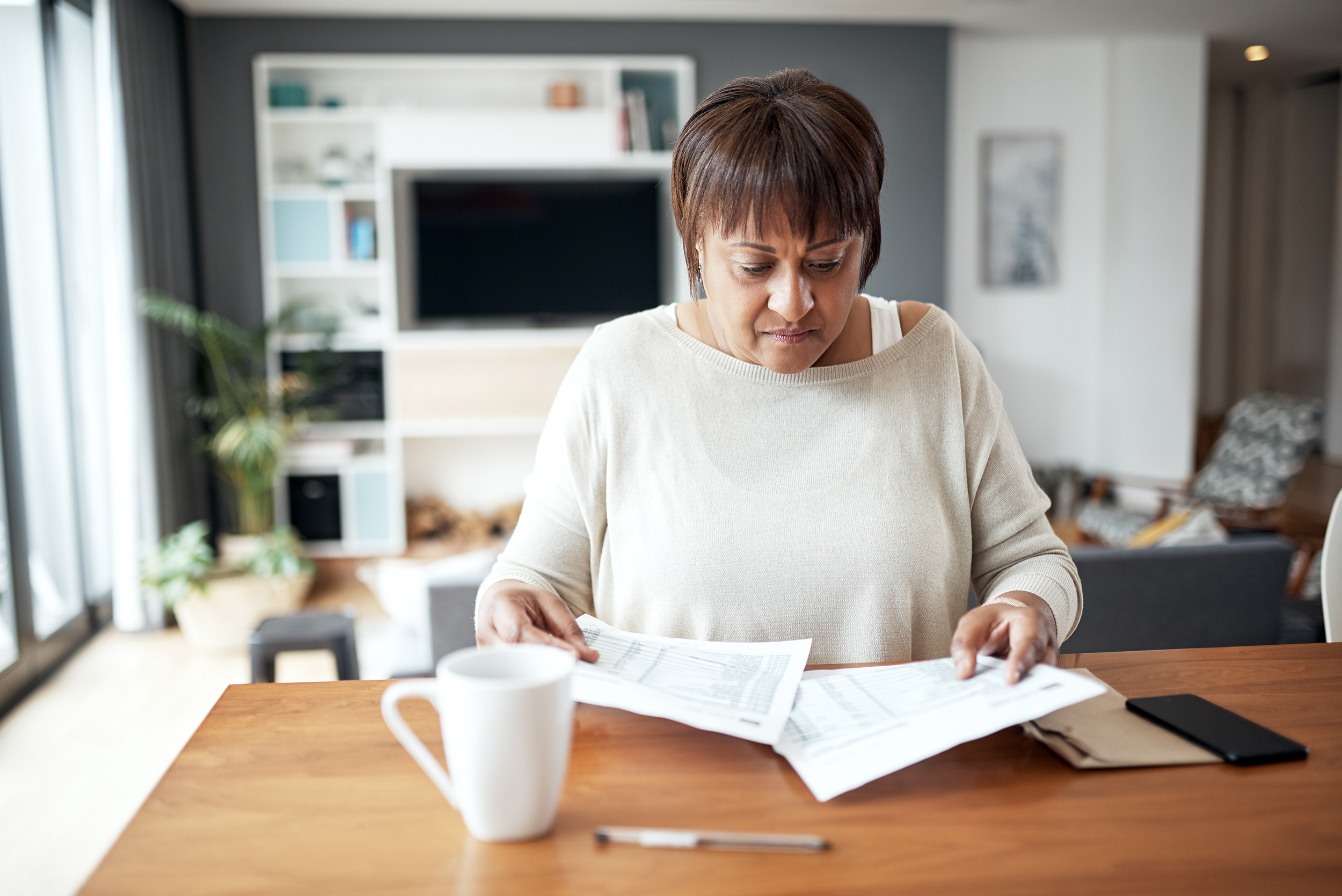 A woman looks over papers on a table in her living room. It's important to prepare for your disability appeal hearing with a Social Security administrative law judge.