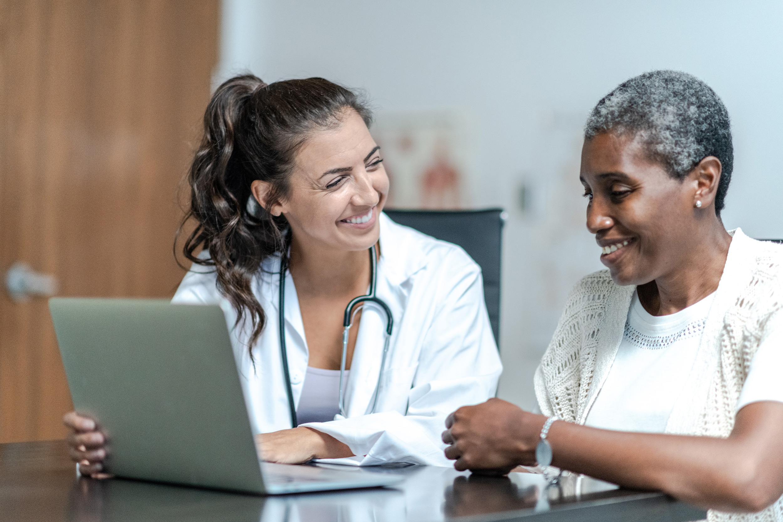 A doctor sits at a table with a laptop, talking to her patient. When you're awarded Social Security Disability due to health problems, you receive back pay to cover time you spent waiting on a decision.