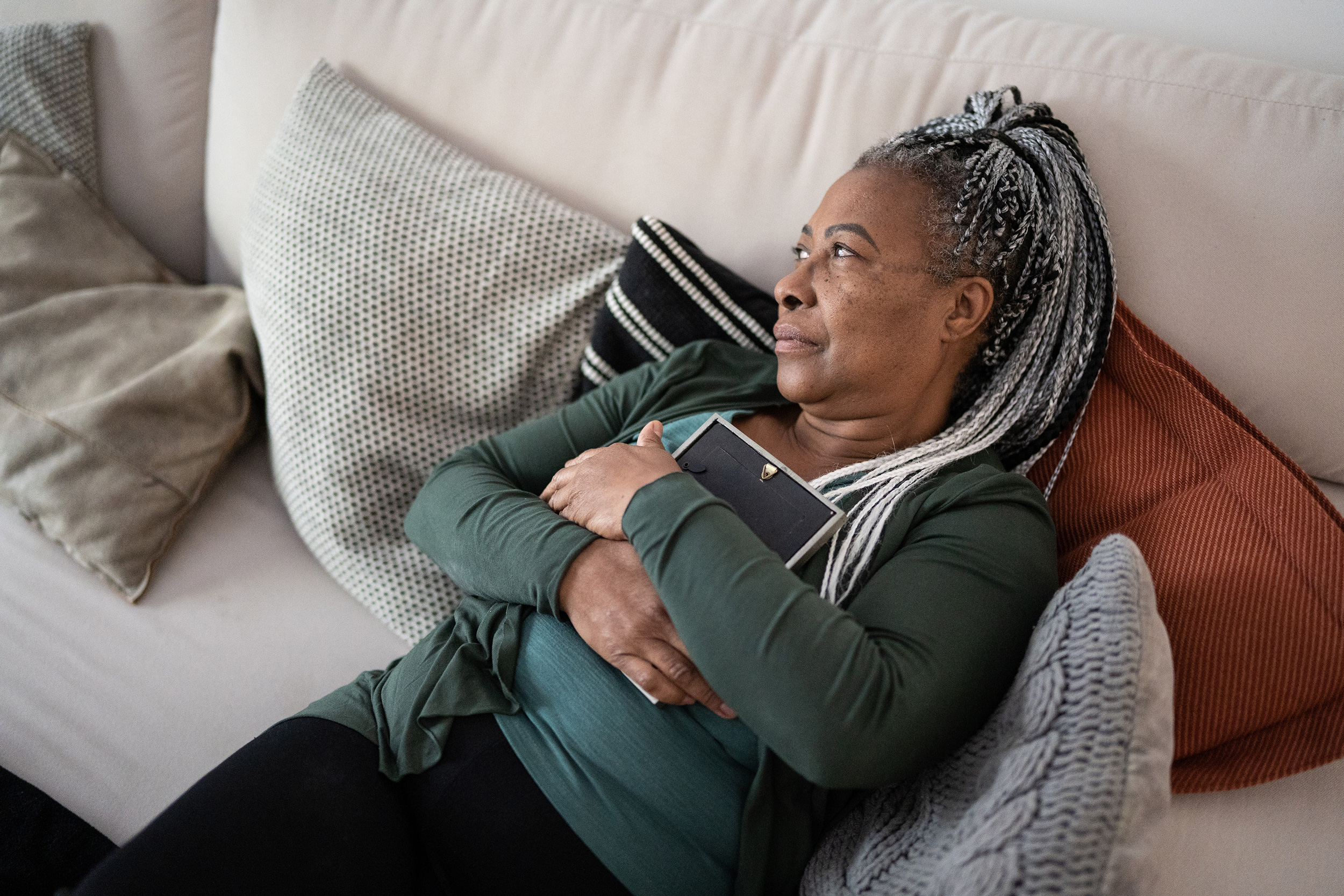 Reclining on her couch, a woman hugs a picture frame. People with certain direct relationships with a deceased Social Security Disability recipient can qualify for survivor benefits.