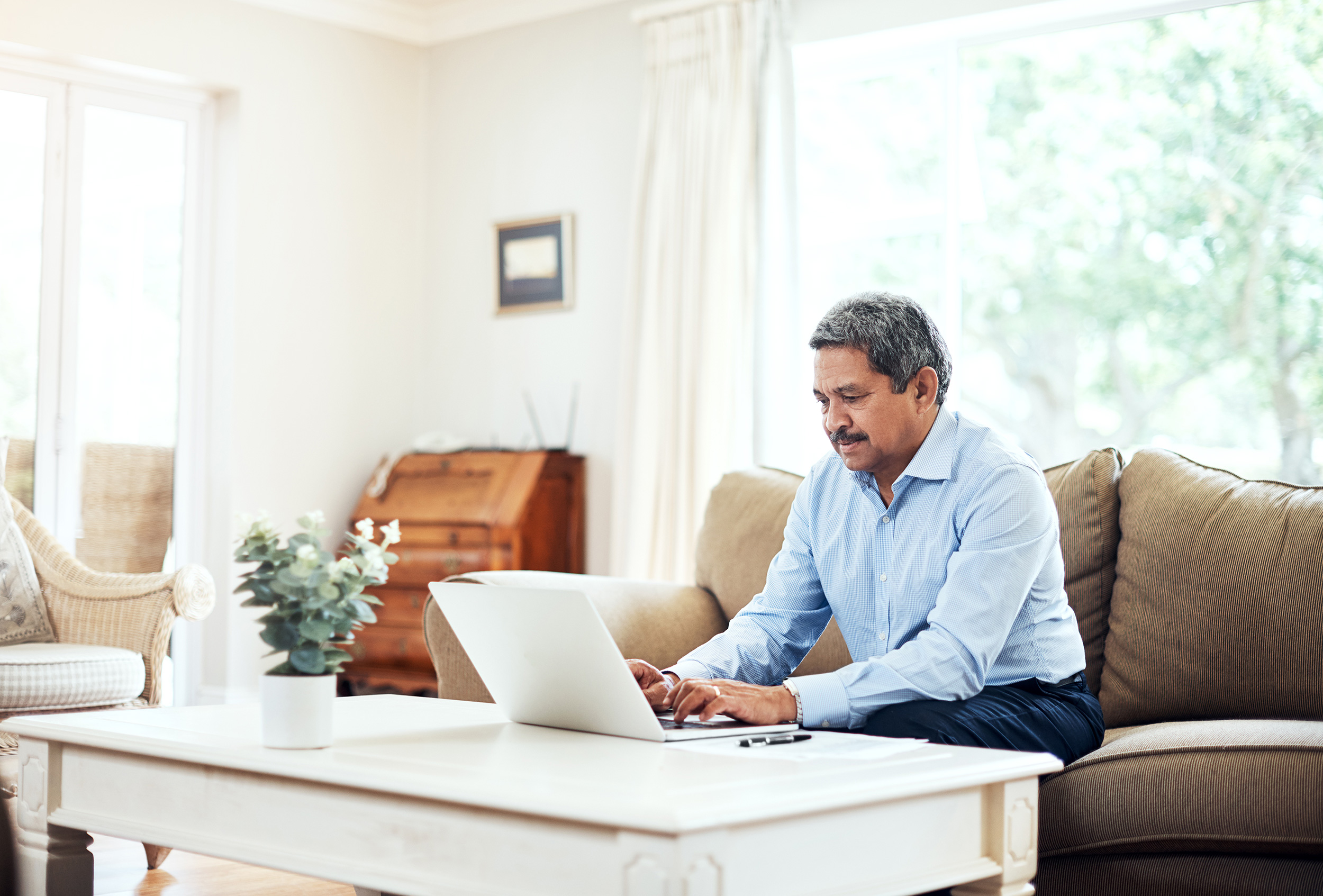 From his couch, a man types on a laptop on his coffee table. A disability lawyer can help you appeal a denial of Social Security Disability benefits.
