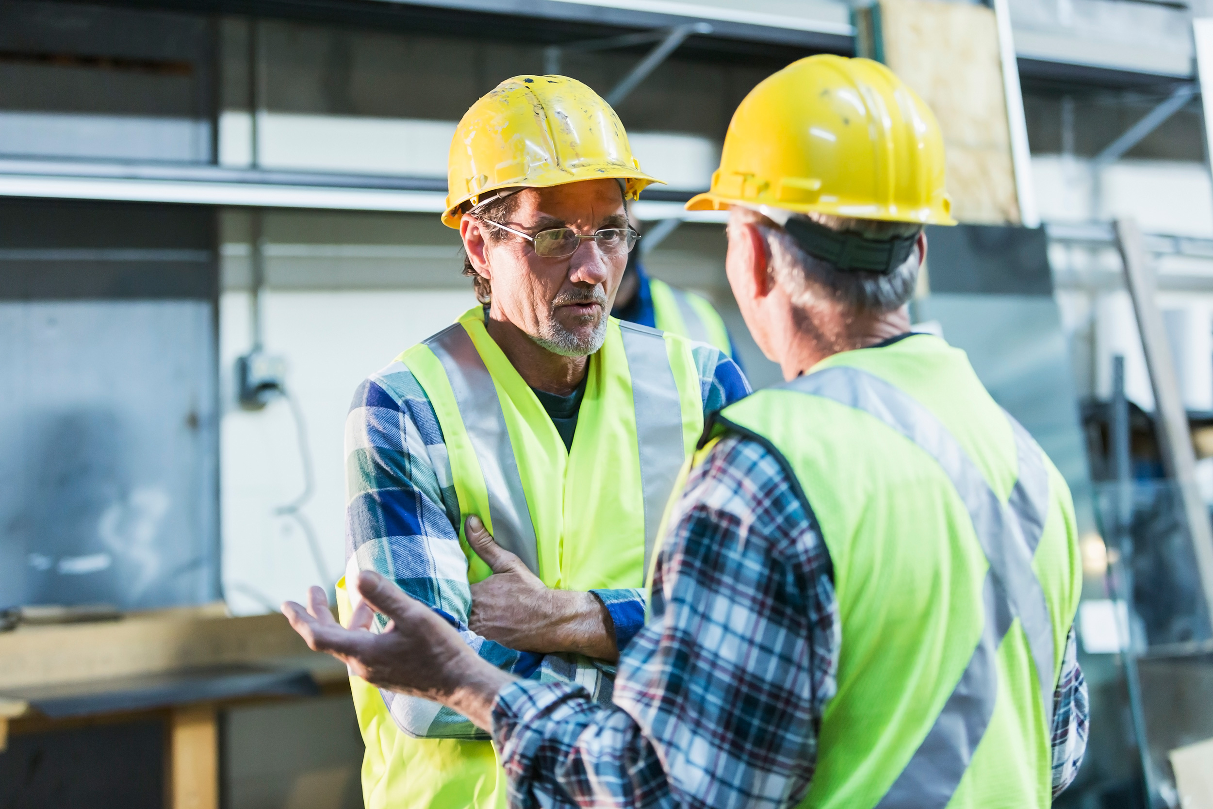 Two men wearing safety vests and hard hats talk to each other on a work site. The qualifications to get SSI disability benefits and SSDI befits vary.