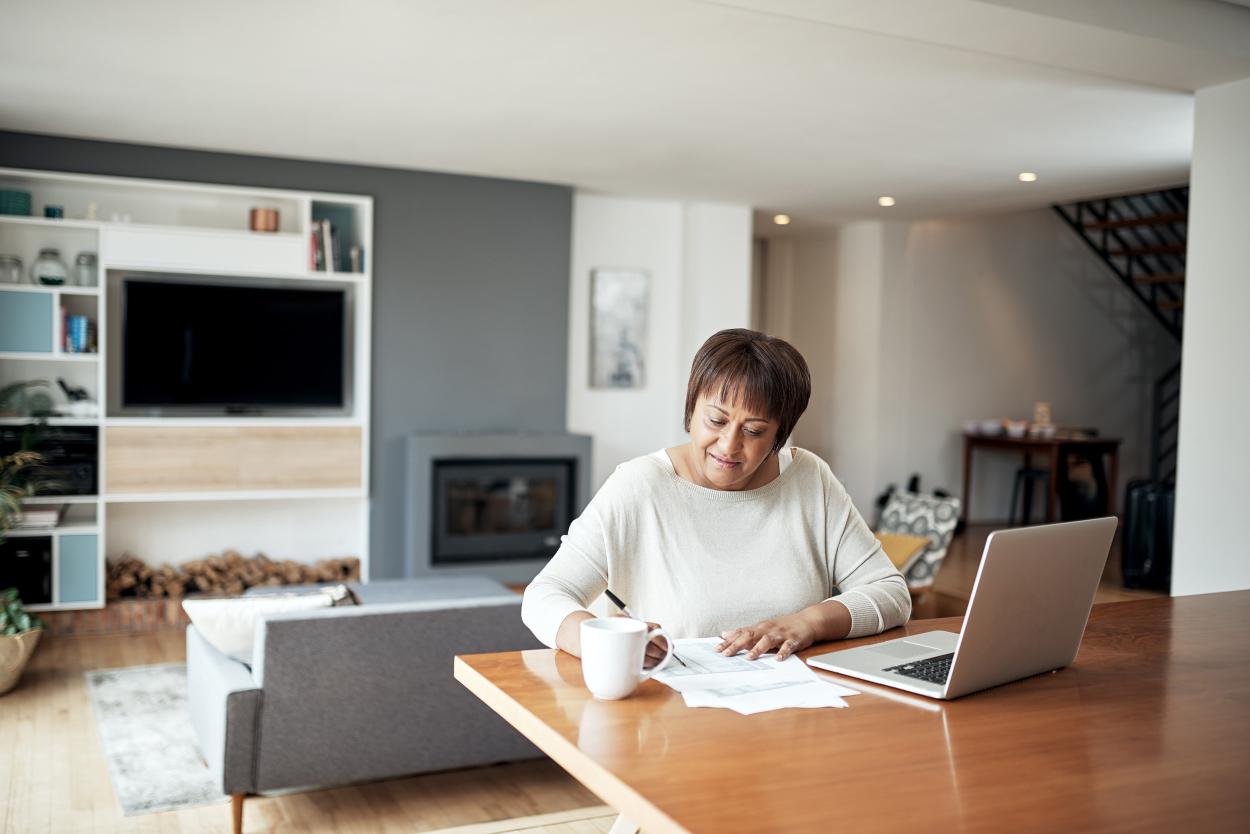 Writing on papers on a table in her home, a woman has her laptop open and coffee mug nearby. A Social Security Disability hearing with a judge looks different from a trial you might see on TV.