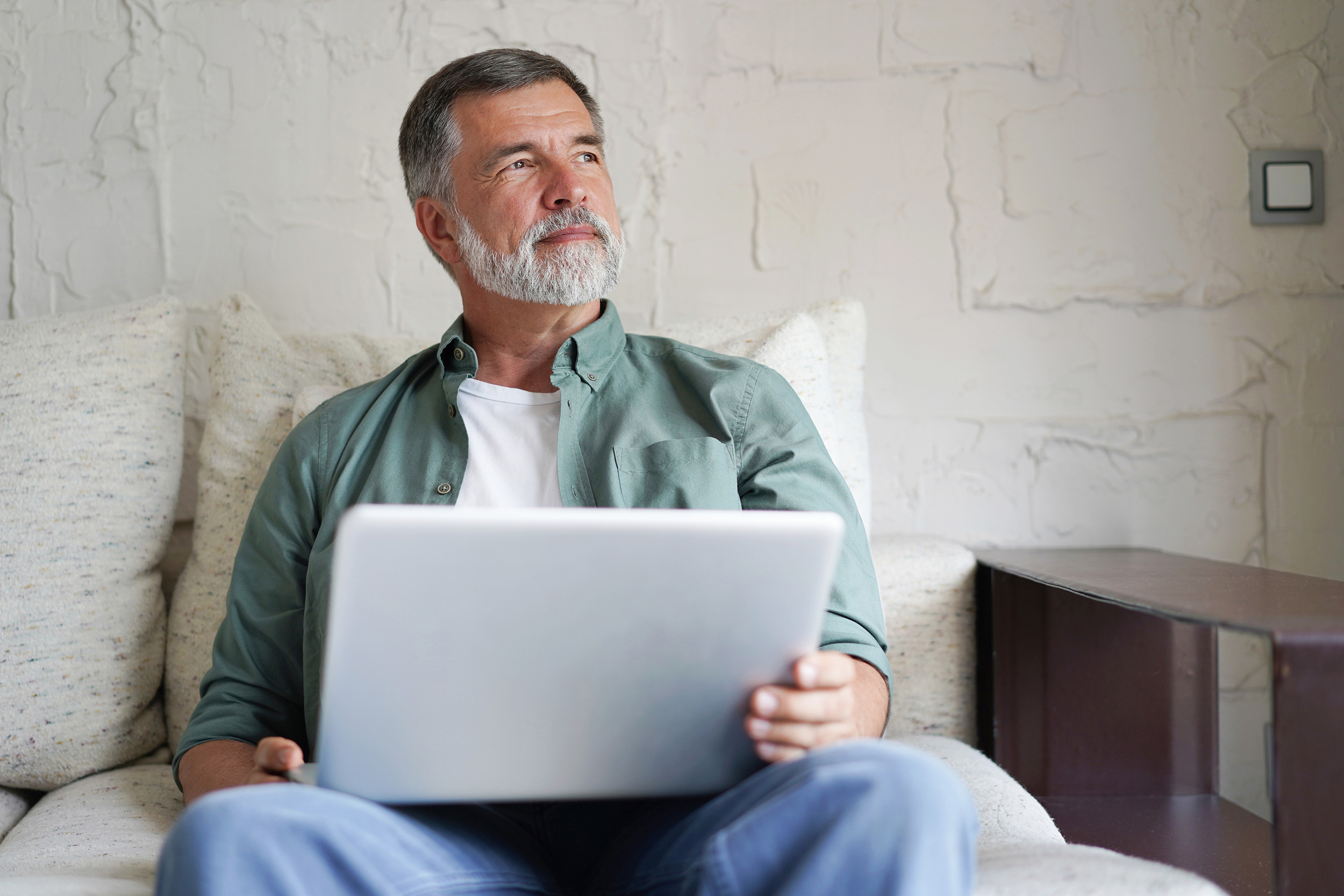 Sitting on his couch, a man looks up from his laptop. Applying for Social Security Disability includes filling out and sending forms to the government.