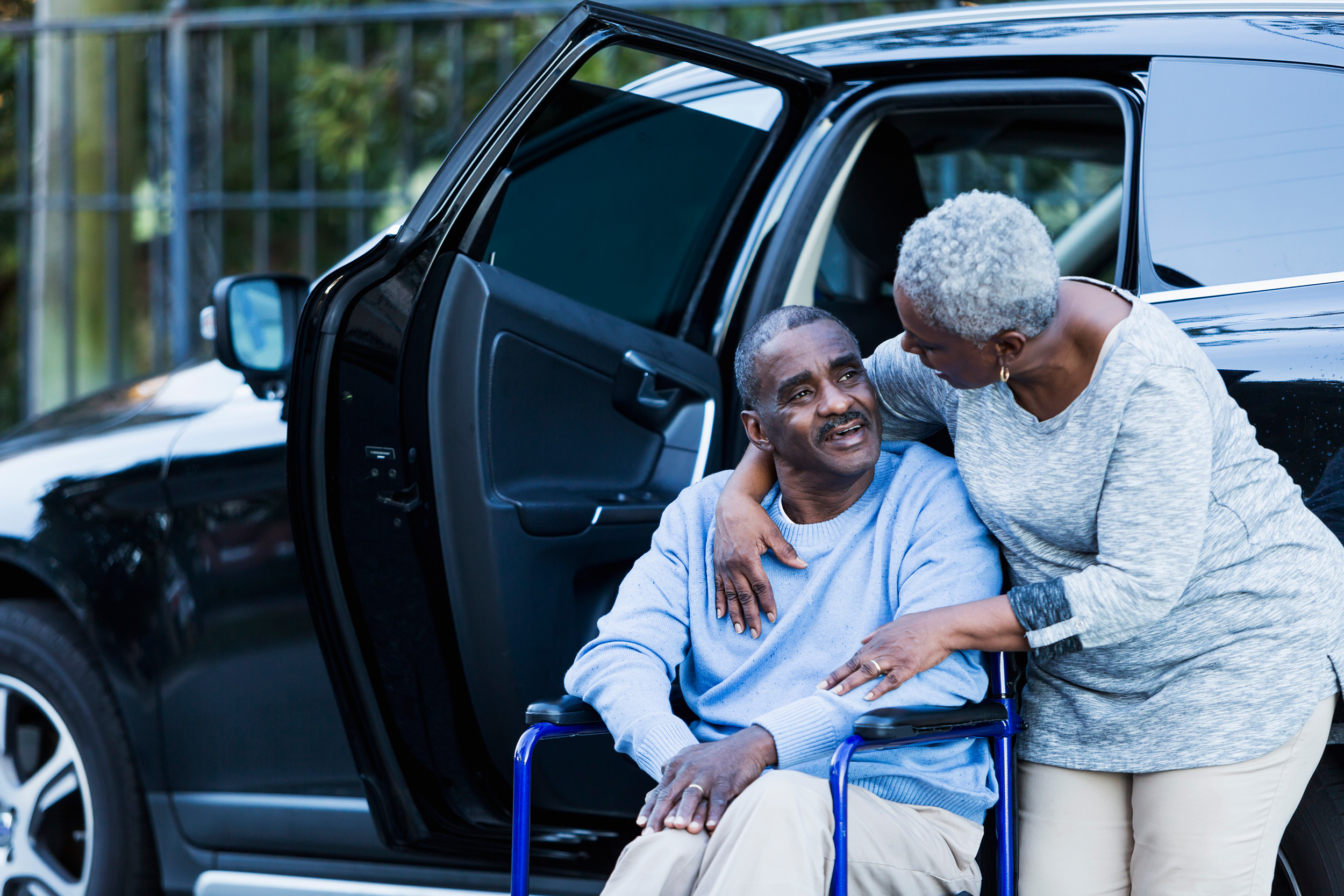 Just outside the open door of their SUV, a woman puts her arm around the shoulder of a man in a wheelchair. Eligibility for SSI benefits includes having serious heath problem, limited income and low financial assets.