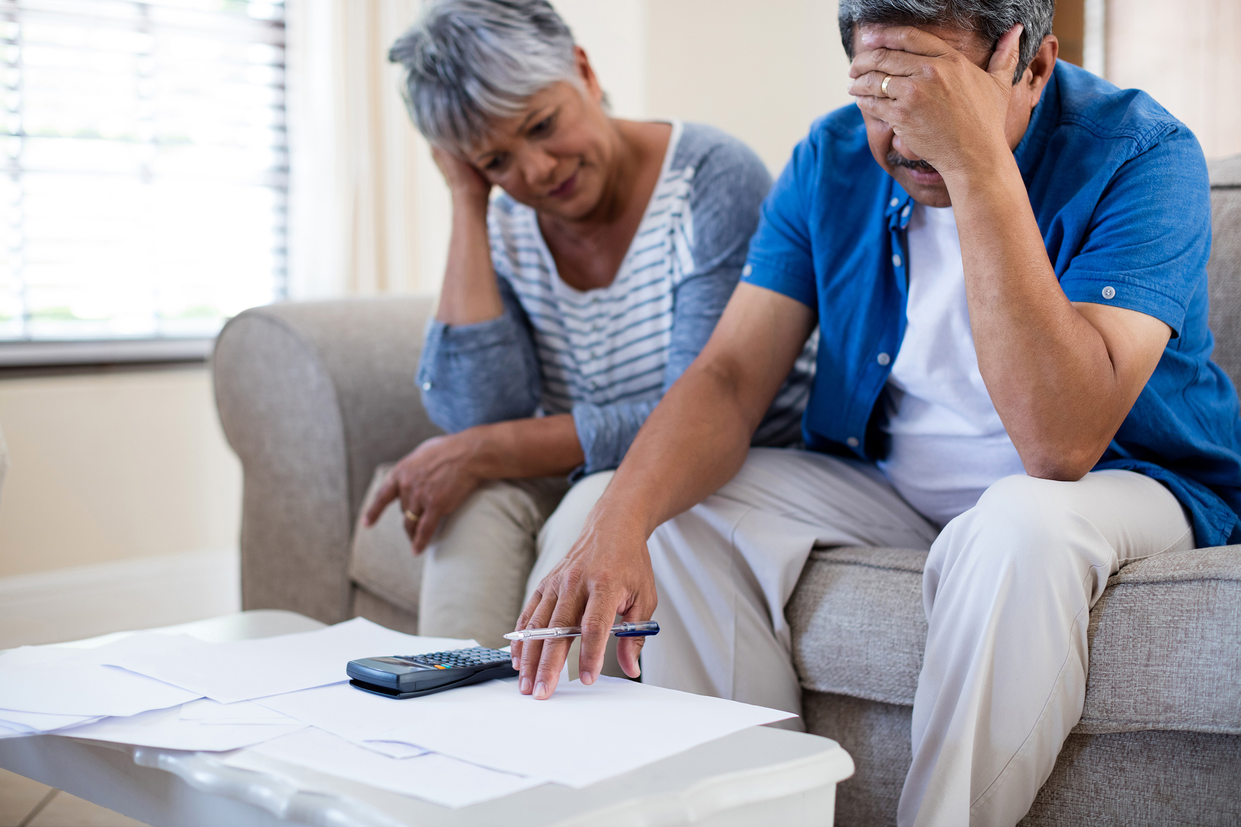 Sitting on a couch with papers and a calculi on a coffee table in front of them, a man and woman make frustrated expressions. Your life average lifetime earnings number goes into calculating your SSDI benefits.