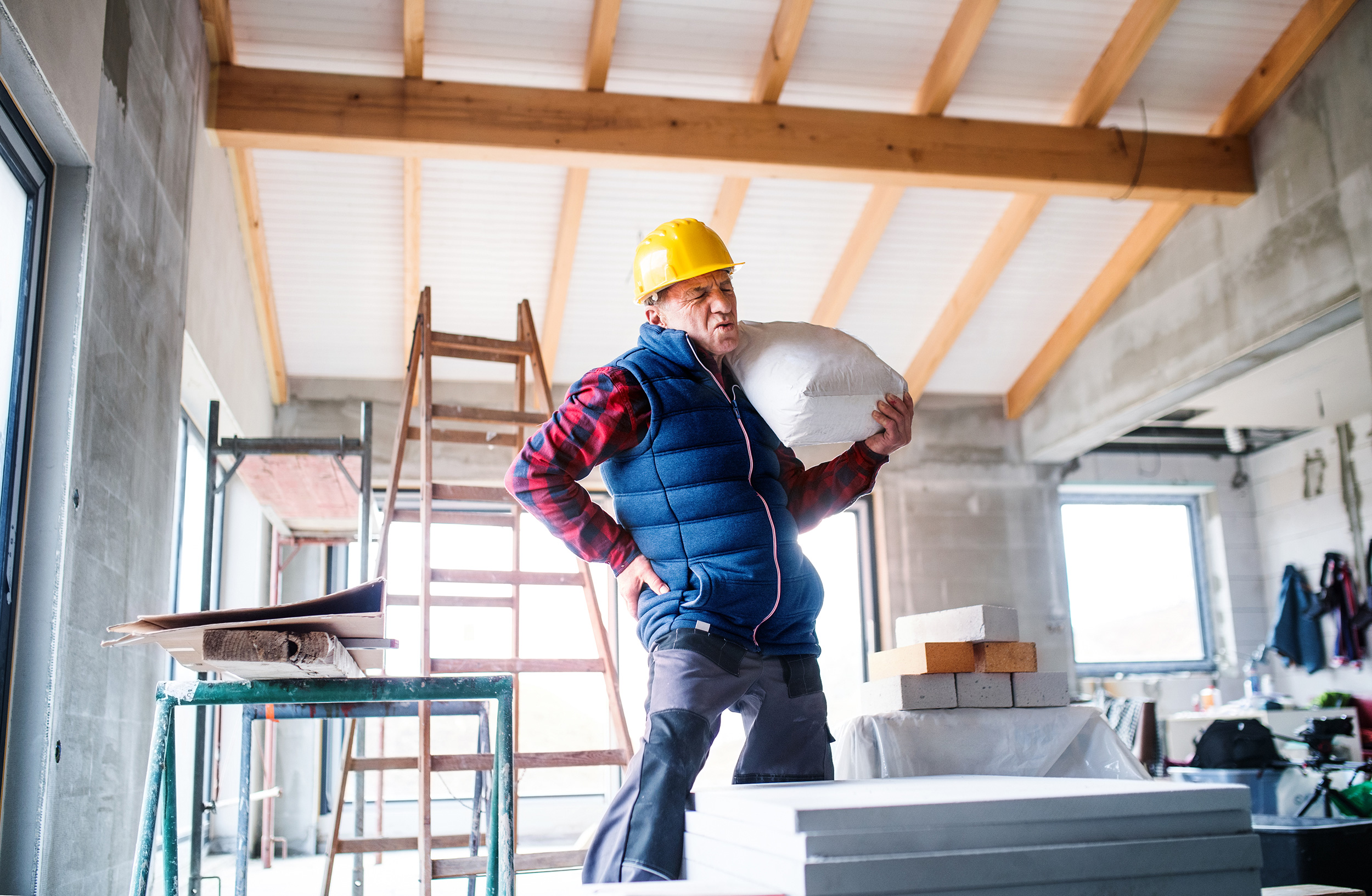 Carrying a heavy bag of materials in an unfinished room, a construction worker grips his back in pain. Social Security Disability lawyers help workers get important benefits.