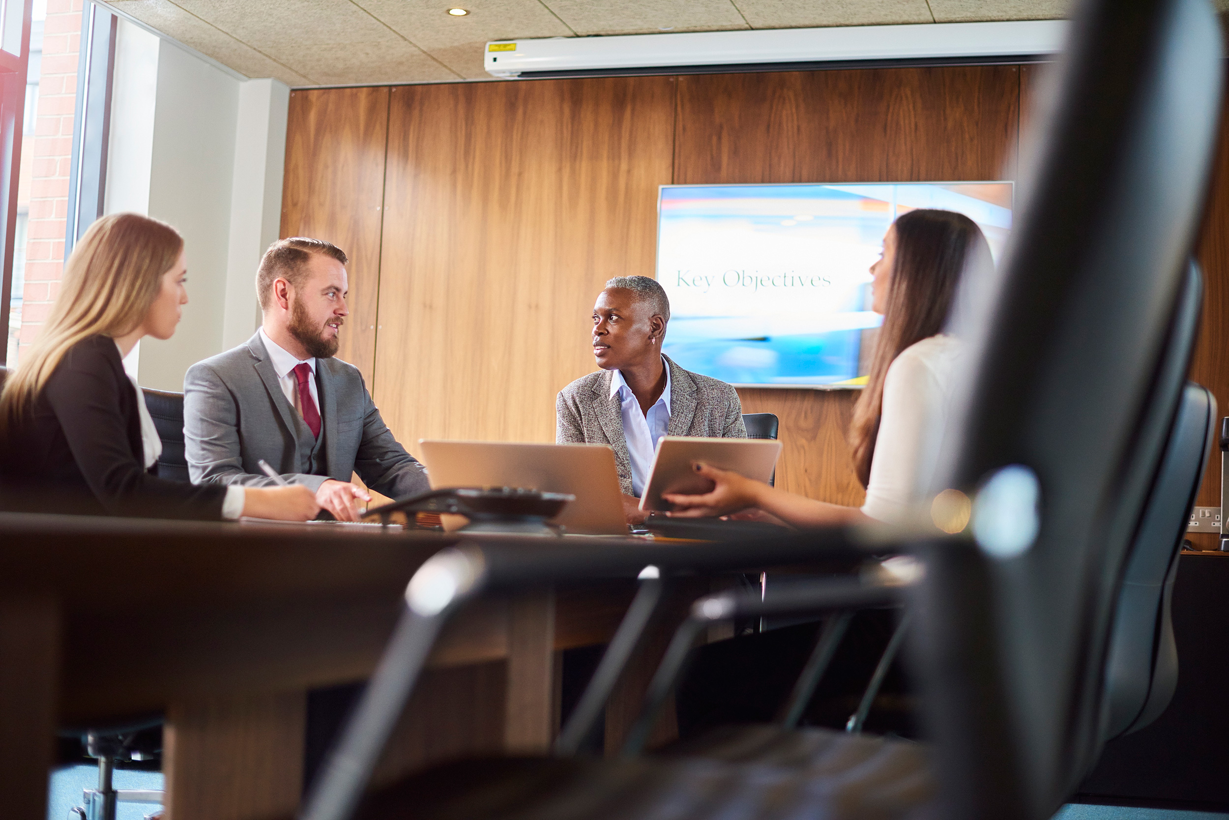 Four people, a man and three women, professionally dressed, talk at a conference room table. Appealing a disability benefits denial can include going to hearings, sending information to government review boards, and even filing a case in federal court.