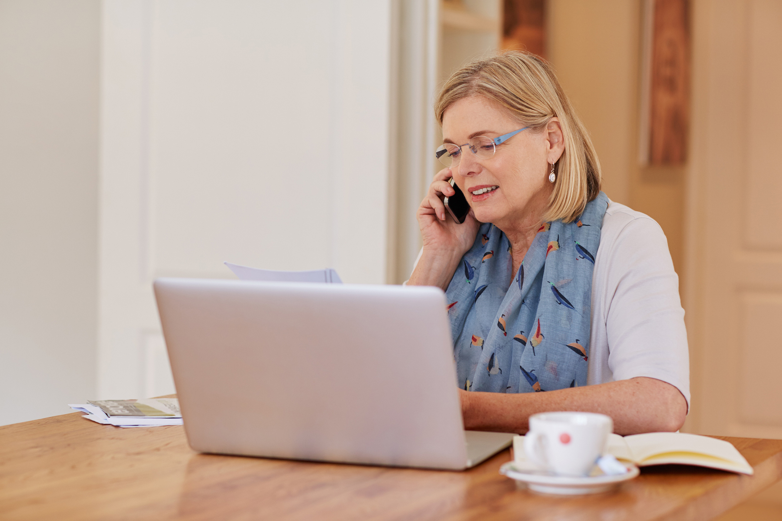 Laptop open, paper in hand and teacup on the table, a woman talks on the phone. Problems with your application paperwork are major possible reasons your Social Security Disability application could be denied.