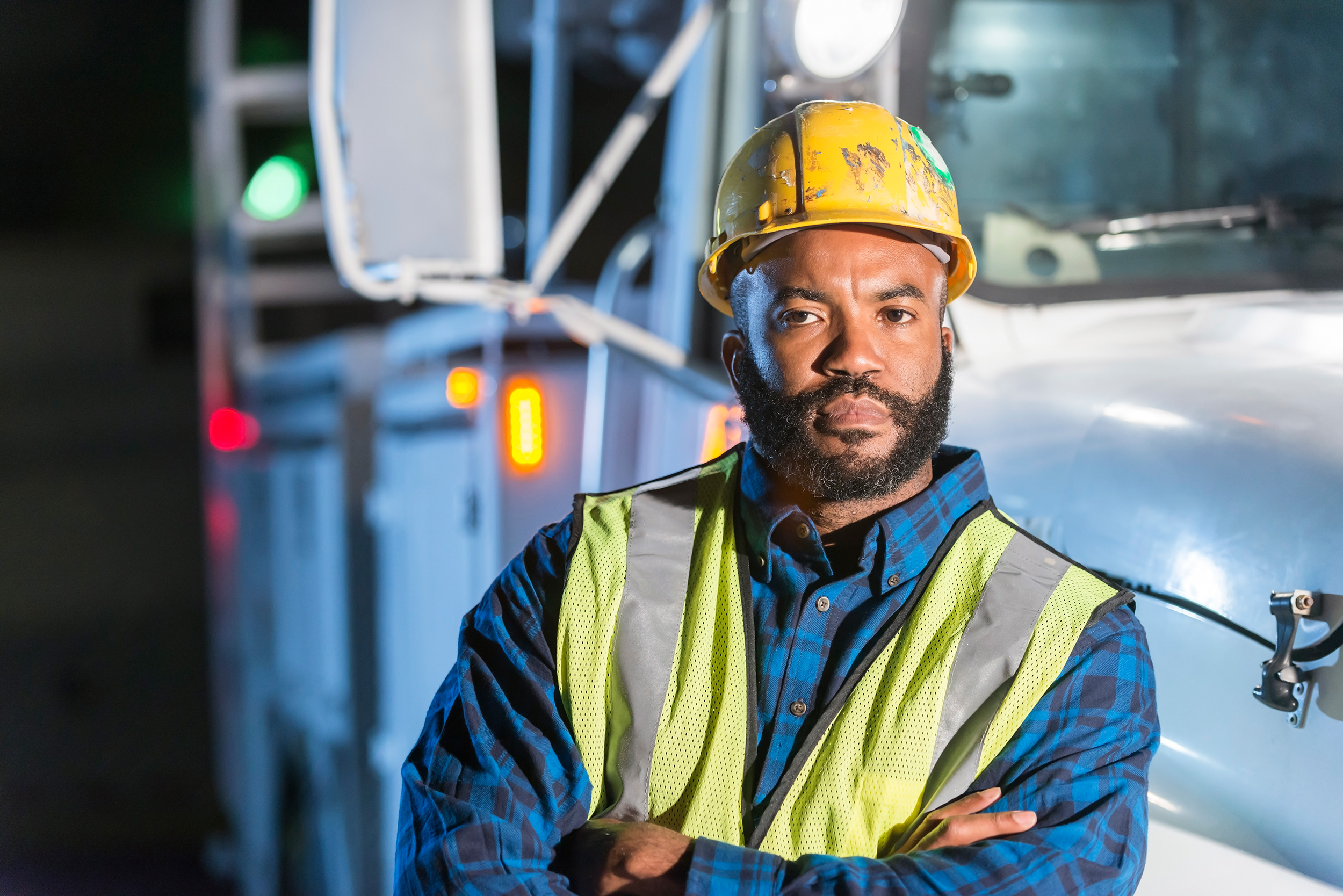 Folding his arms and wearing a safety vest and helmet, a man stands in front of a work truck at night. If you're able to work enough to equal what Social Security calls "substantial gainful activity," you may be denied disability benefits.