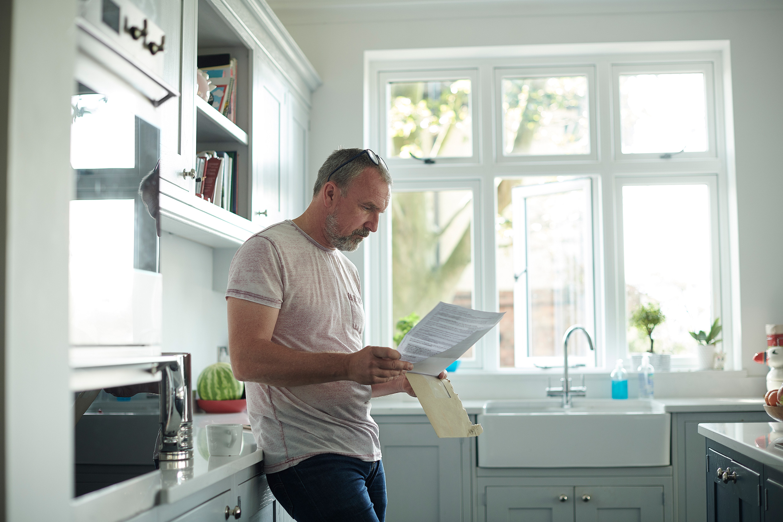 A man leans against his kitchen countertop reading paperwork. The attorneys at Troutman & Troutman help people in Tahlequah qualify for disability benefits.