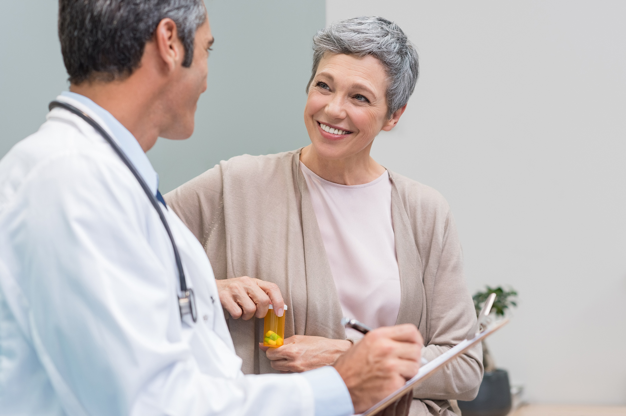 Holding a pill bottle, a woman sits next to a doctor with a clipboard and smiles at him. You need certain forms of evidence and information to qualify for disability benefits.