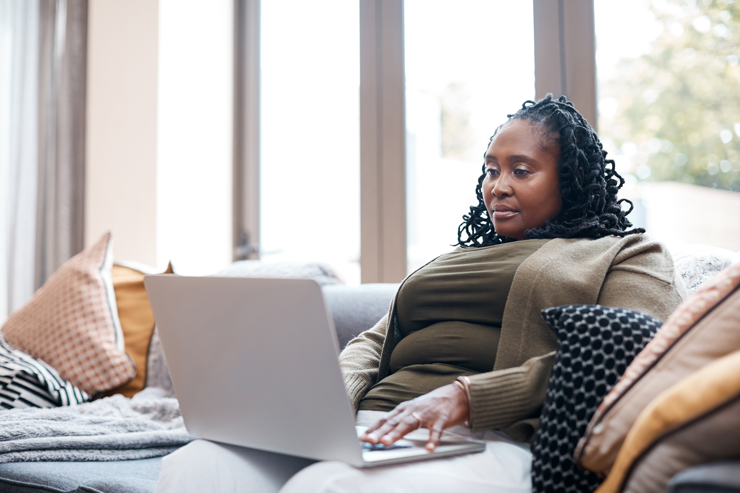 A woman reclines on a couch in front of a window, typing on her laptop. Troutman & Troutman disability lawyers answer questions about disability benefits every day.