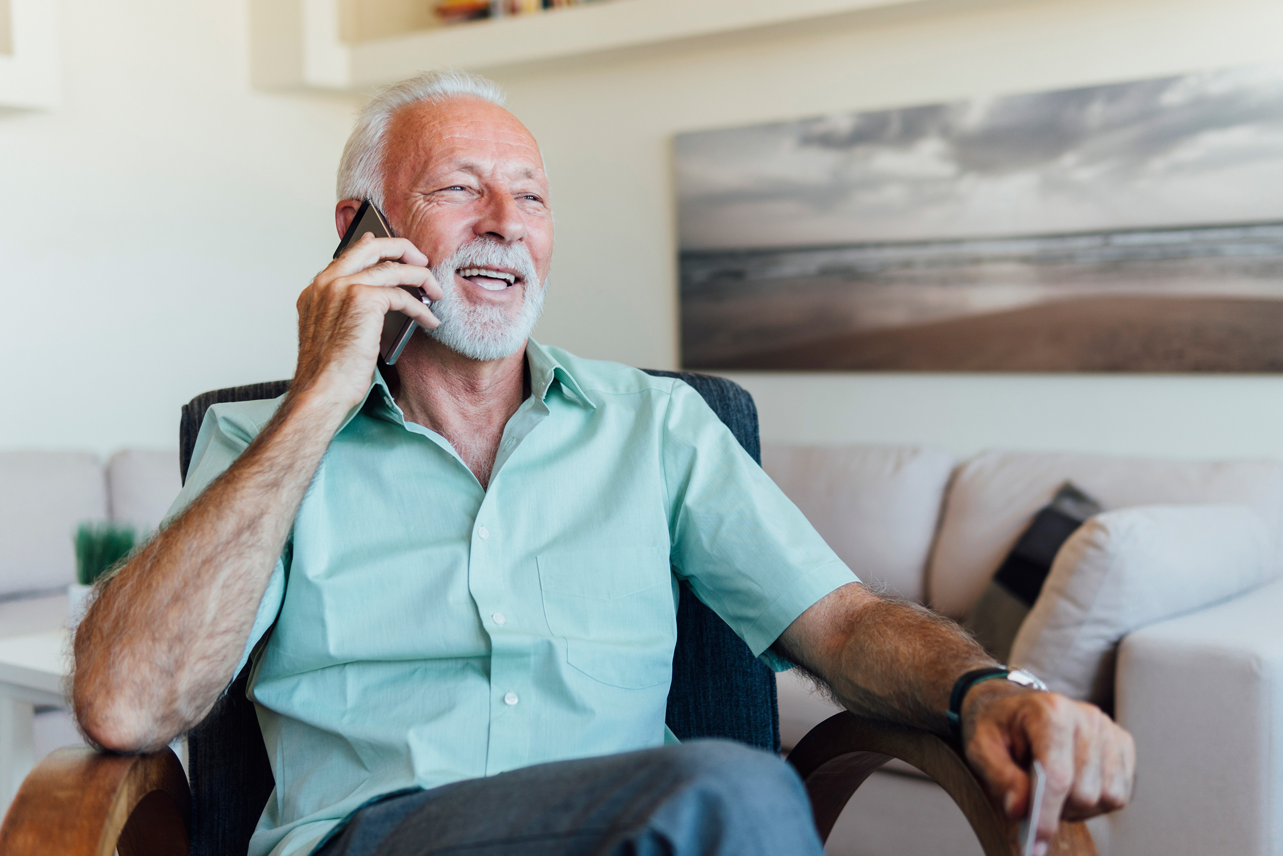 A man smiles as he sits in a chair and talks on a phone. Troutman & Troutman disability lawyers answer questions about disability benefits every day.