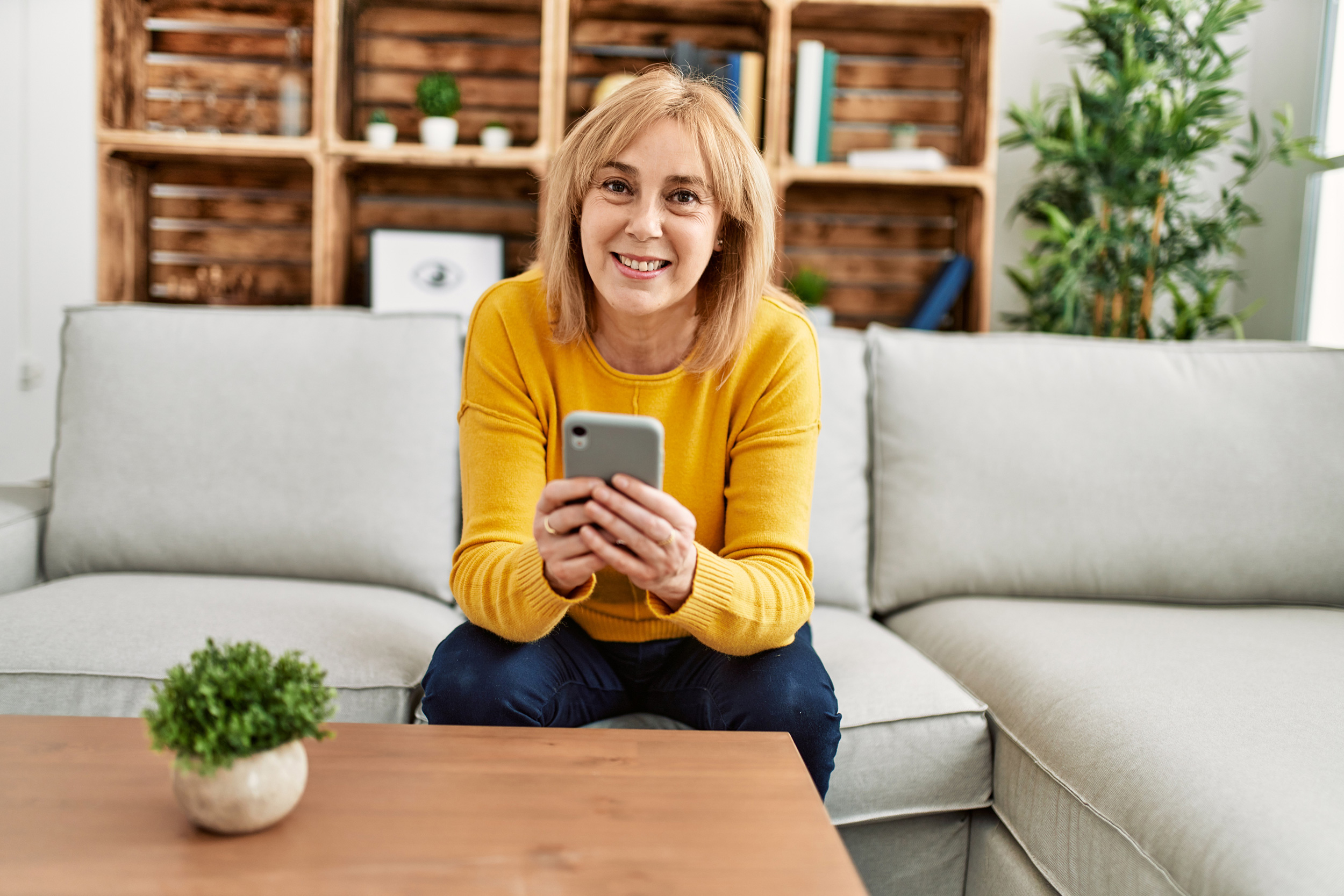 Leaning forward on her couch, a woman holds her smartphone in both hands and looks up. Troutman & Troutman['s Oklahoma disability lawyers answer questions about disability benefits every day.