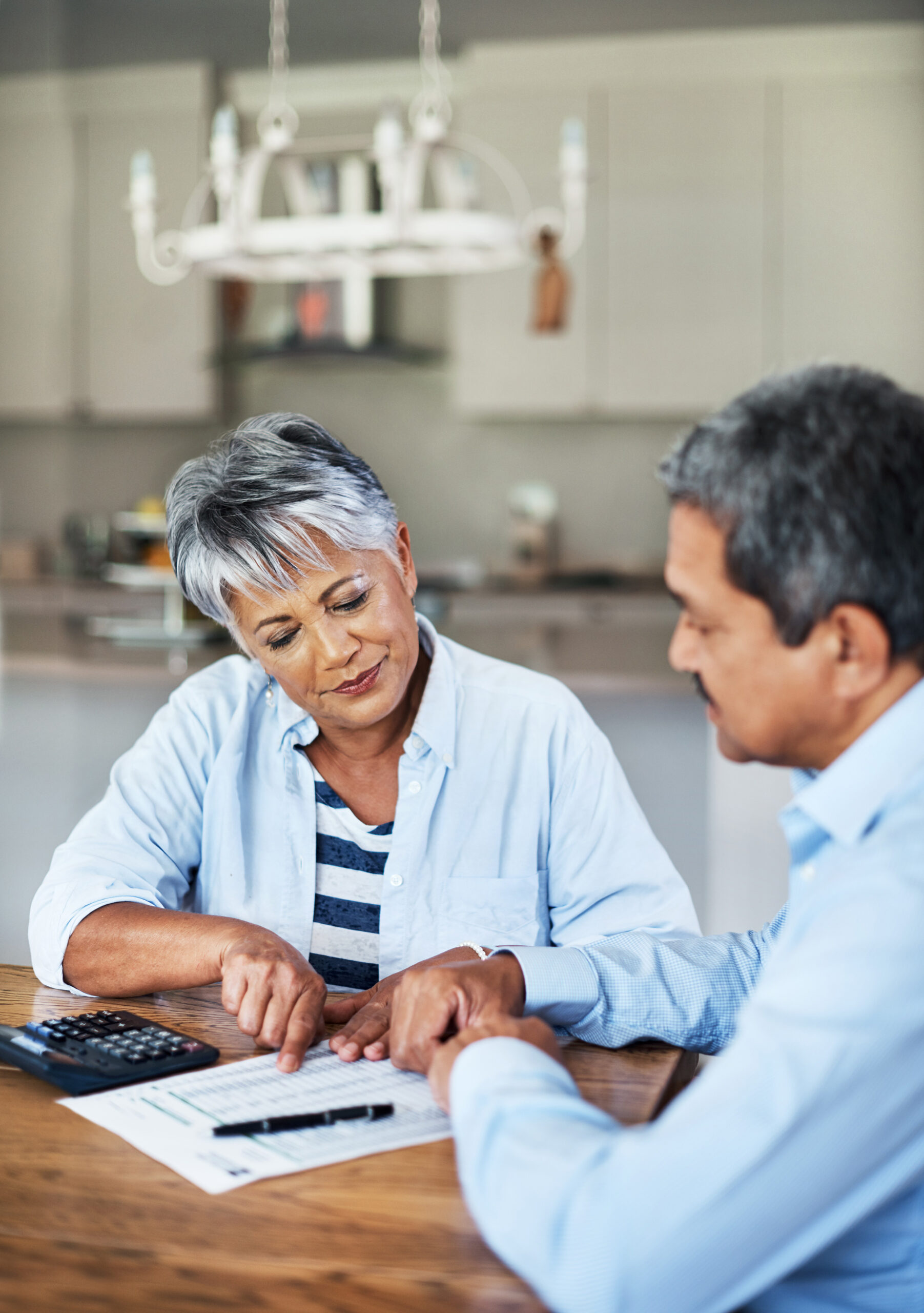 A woman points out numbers on a chart while sitting at a kitchen table with a man. Troutman & Troutman's Oklahoma disability lawyers answer questions about disability benefits every day.