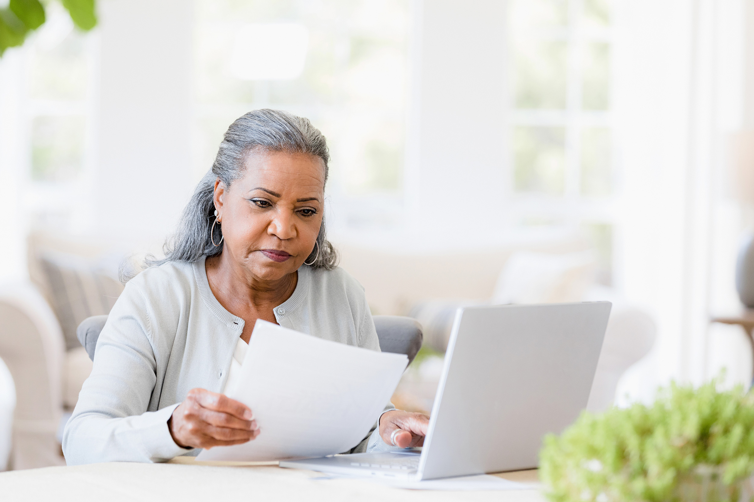 With a concerned expression on her face, a woman looks through papers and a computer. Troutman & Troutman's Oklahoma disability lawyers answer questions about disability benefits every day.