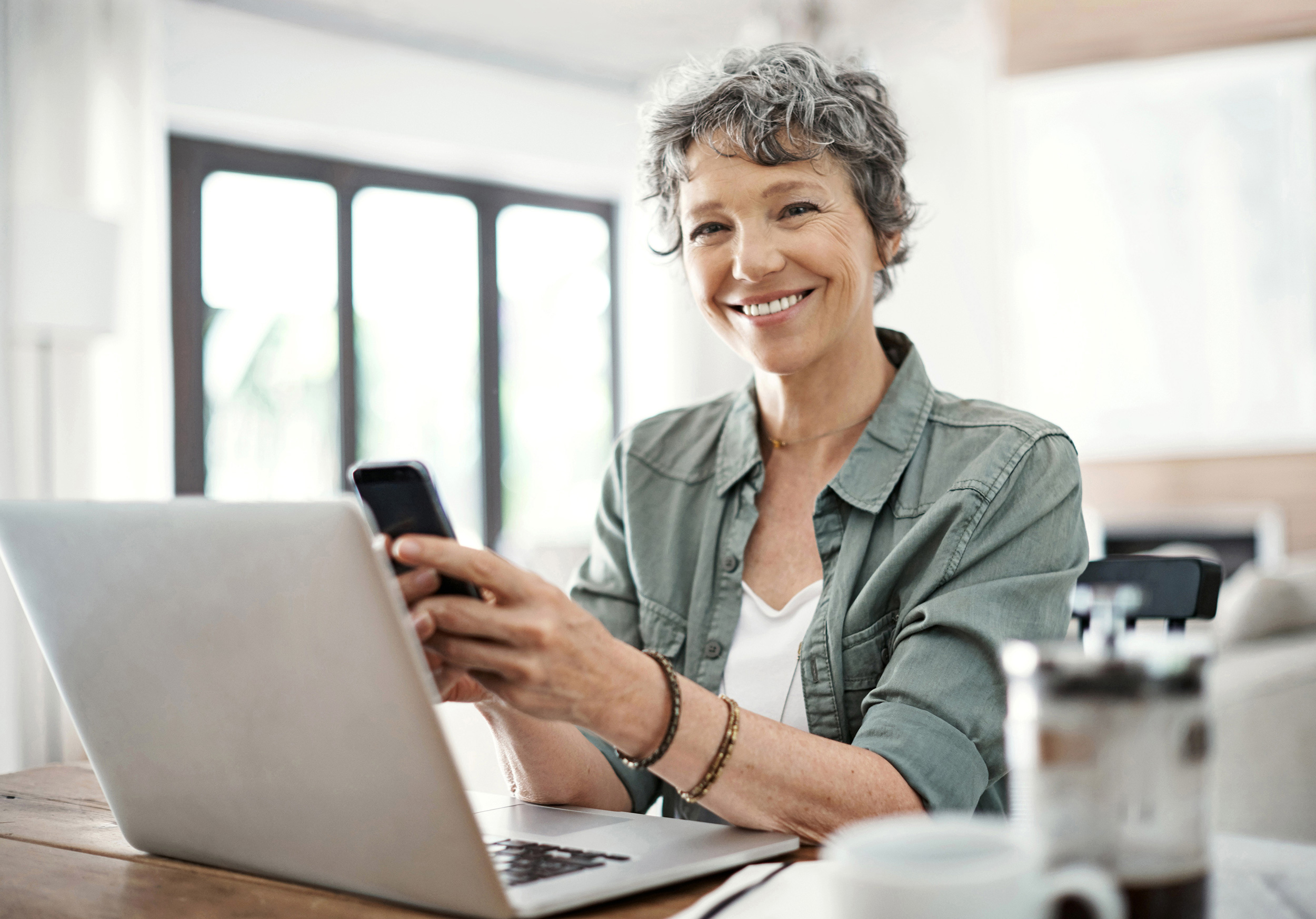 Holding a smartphone while sitting at a computer, a woman smiles. Troutman & Troutman's Oklahoma disability lawyers answer questions about disability benefits every day.