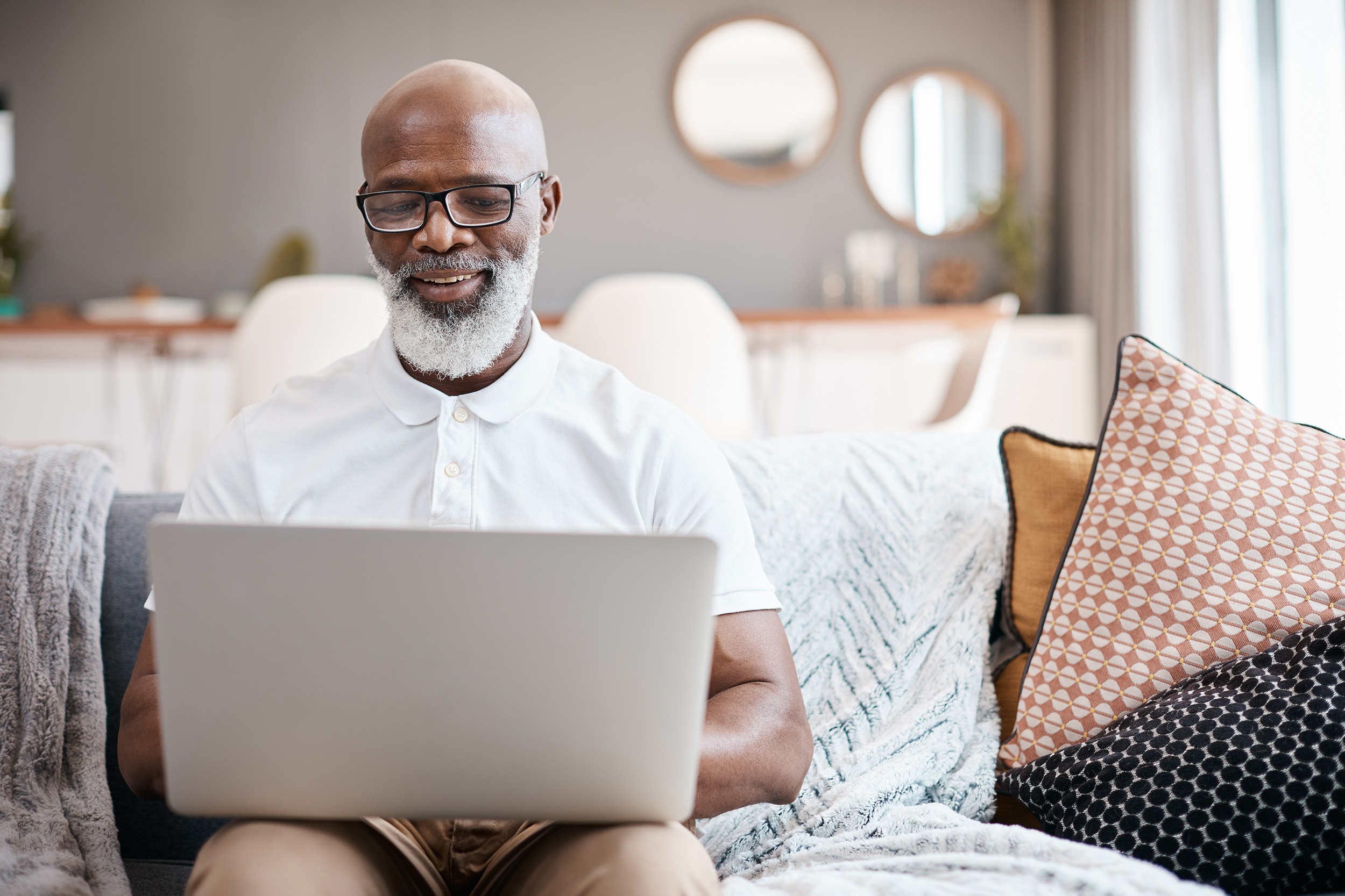 Grinning while he looks at the screen, man sites on a couch typing on his laptop. Troutman & Troutman disability lawyers answer questions about disability benefits every day.