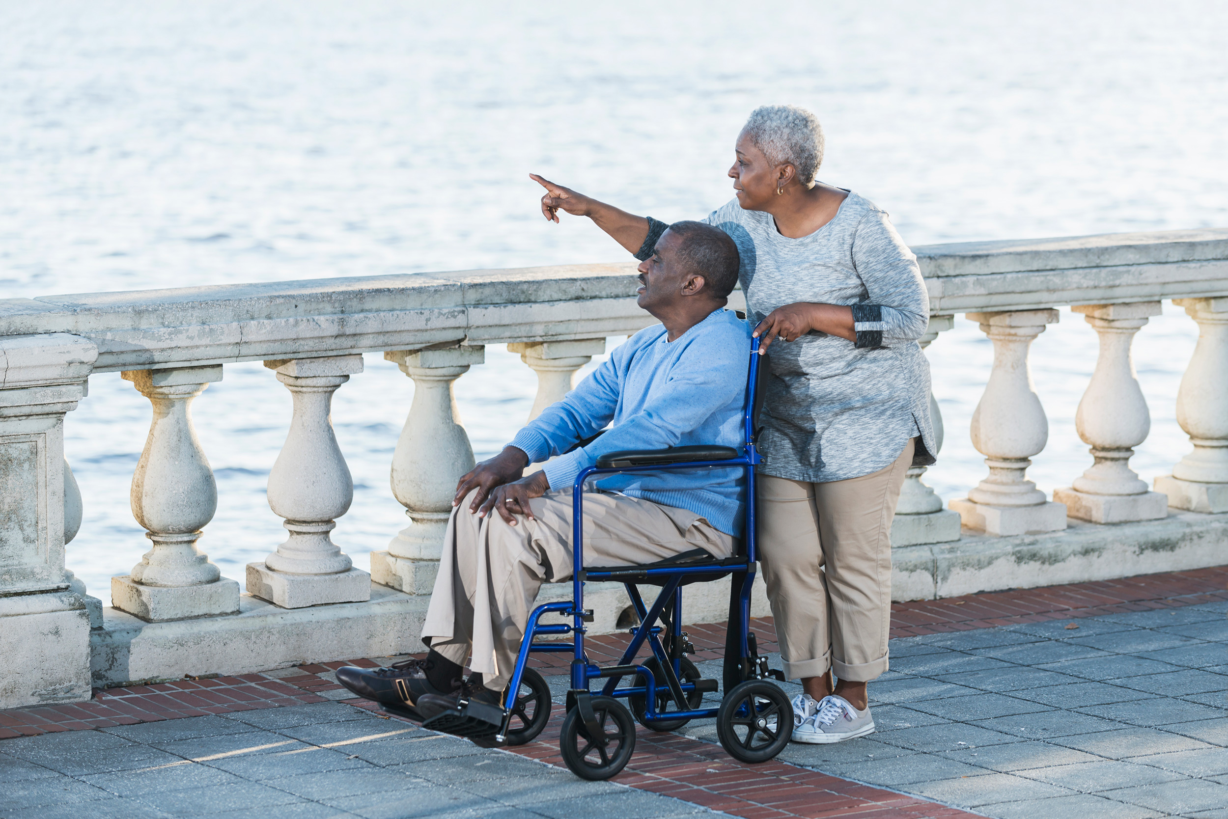 Standing on a patio overlooking a body of water, a woman points something out to a man in a wheelchair. Troutman & Troutman's Oklahoma disability lawyers answer questions about disability benefits every day.