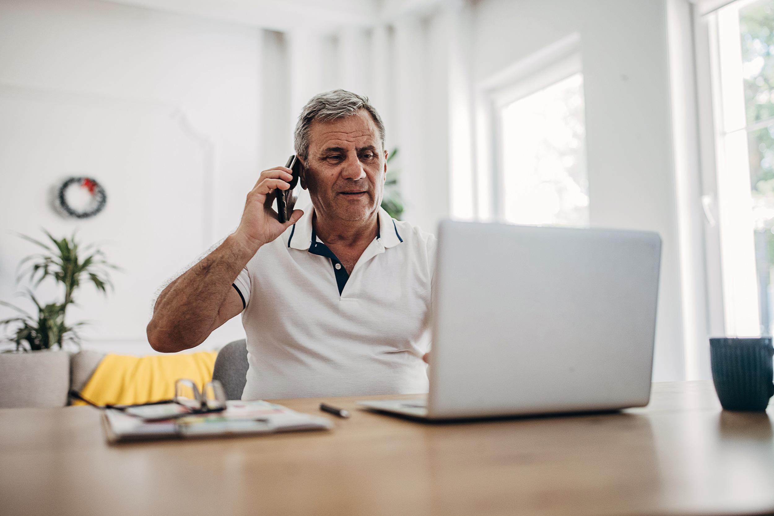 Sitting at a computer at a table, a man talks on a smartphone. Troutman & Troutman disability lawyers answer questions about disability benefits every day.